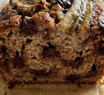 Angeschnittenes Bananenbrot mit Schokoladenstücken auf einem Holzbrett, saftige Krume sichtbar